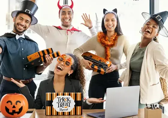 Coworkers in Halloween costumes laughing together in the office while holding Sugarwish gift boxes