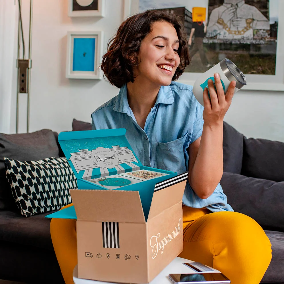 Woman smiling while opening a Sugarwish gift box on her couch
