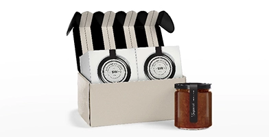 cream-and-black-striped-gift-box-with-jars-of-jam-in-a-box-and-one-jar-of-a-red-colored-jam-sitting-next-to-the-box